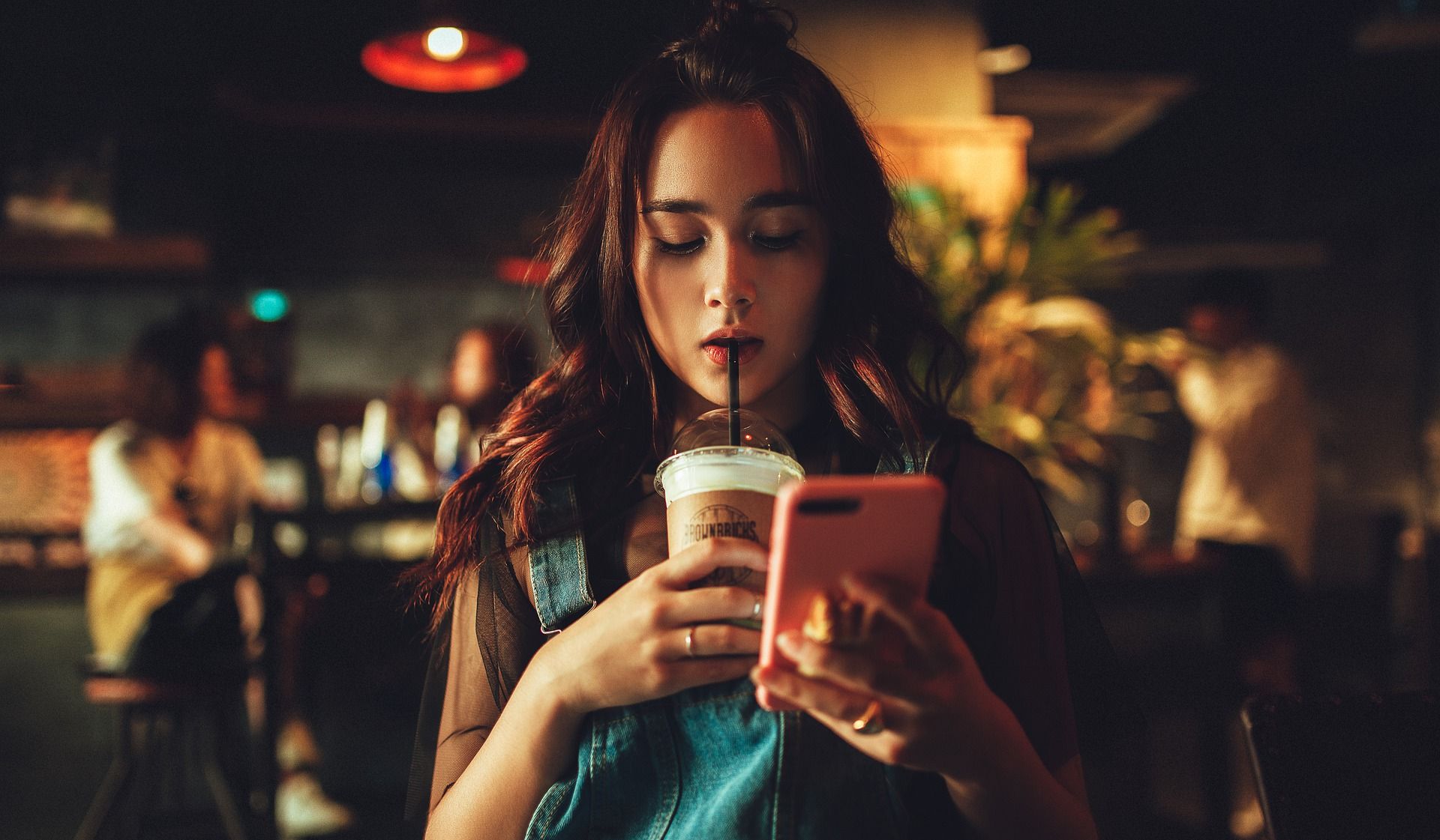 Girl looking at an iPhone and drinking an iced coffee