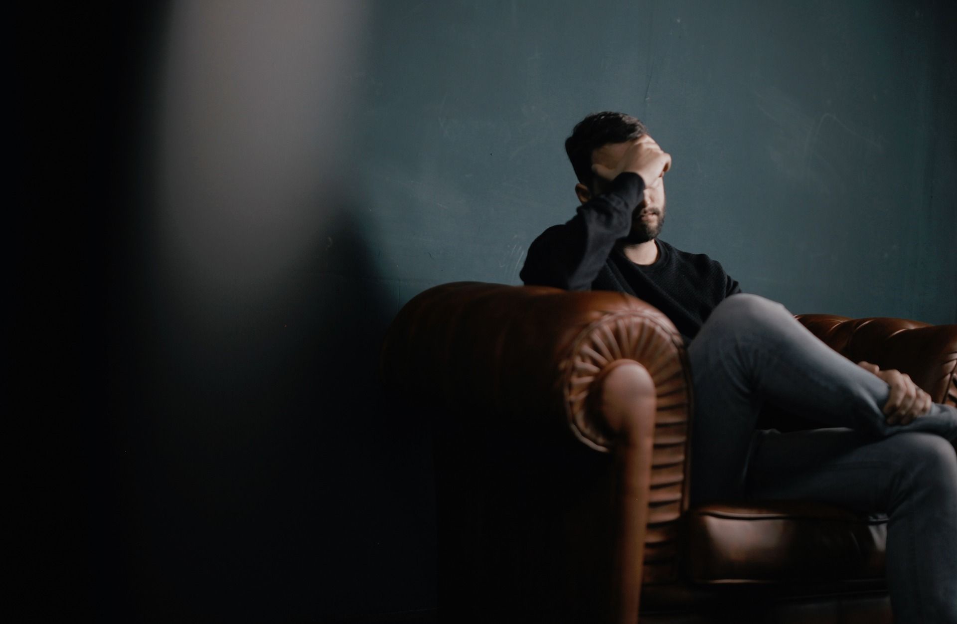 A stressed man with his head in his hand sat cross legged on a chesterfield