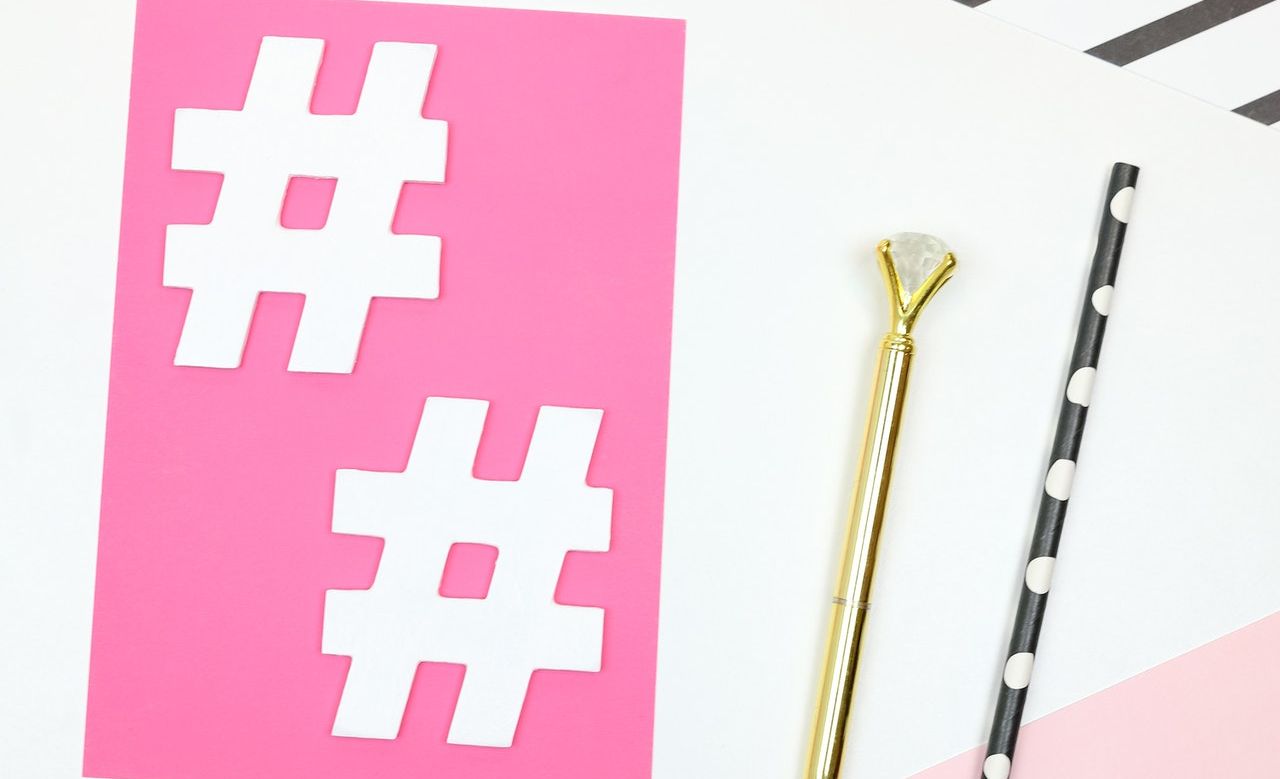 A desk with paper cutouts of hashtag symbols in white laying over pink paper